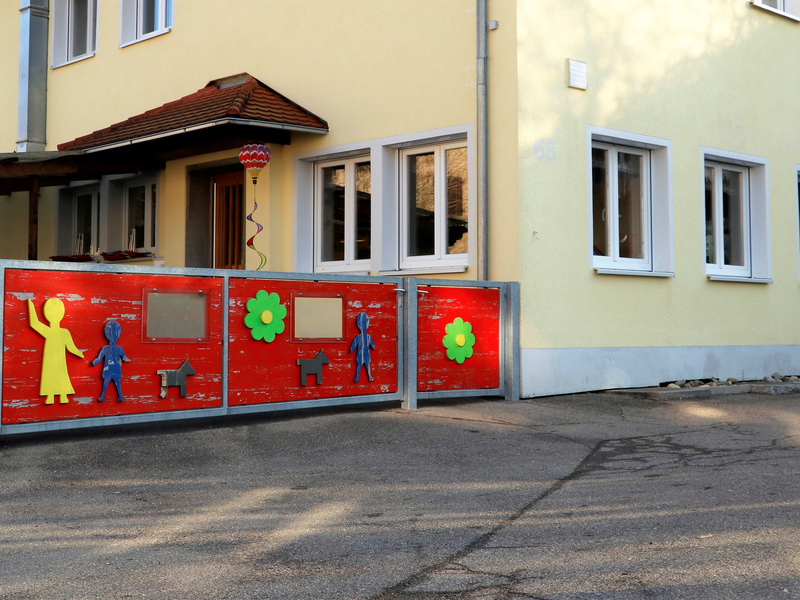 Ein gelbes Gebäude mit einem roten Zaun, der mit bunten Figuren und Blumen verziert ist.