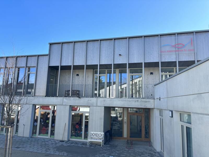 Ein modernes Gebäude aus Beton und Holz mit vielen Fenstern, die mit Fensterbildern geschmückt sind. 